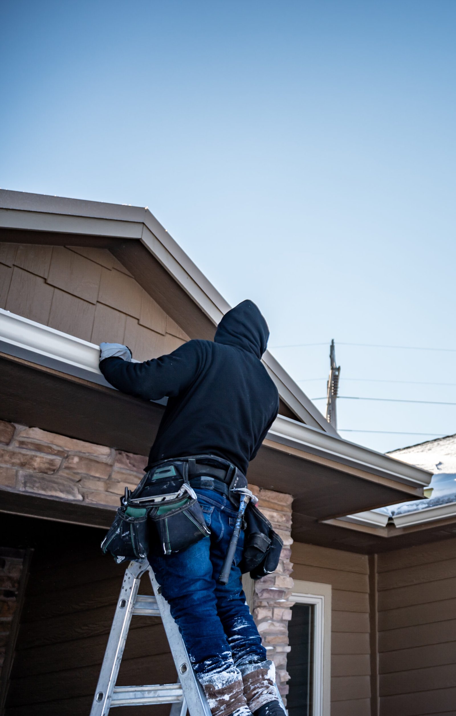 Roofing contractor installing gutters on a residential building in the winter with snow on the roof in Ajax, On