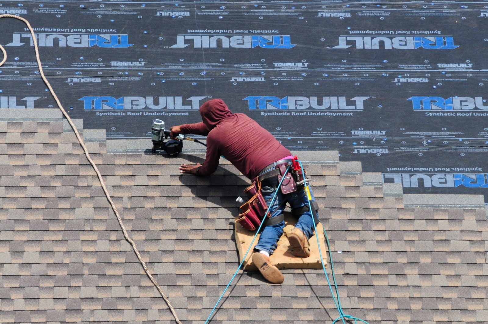 ajax-roof-repair Roofer at work using a pneumatic nail gun to install new shingles on a house roof in Ajax